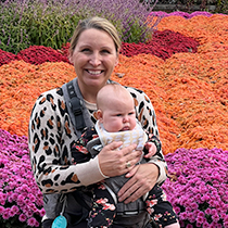 Doctor Megan holding grumpy baby with field of flowers in background
